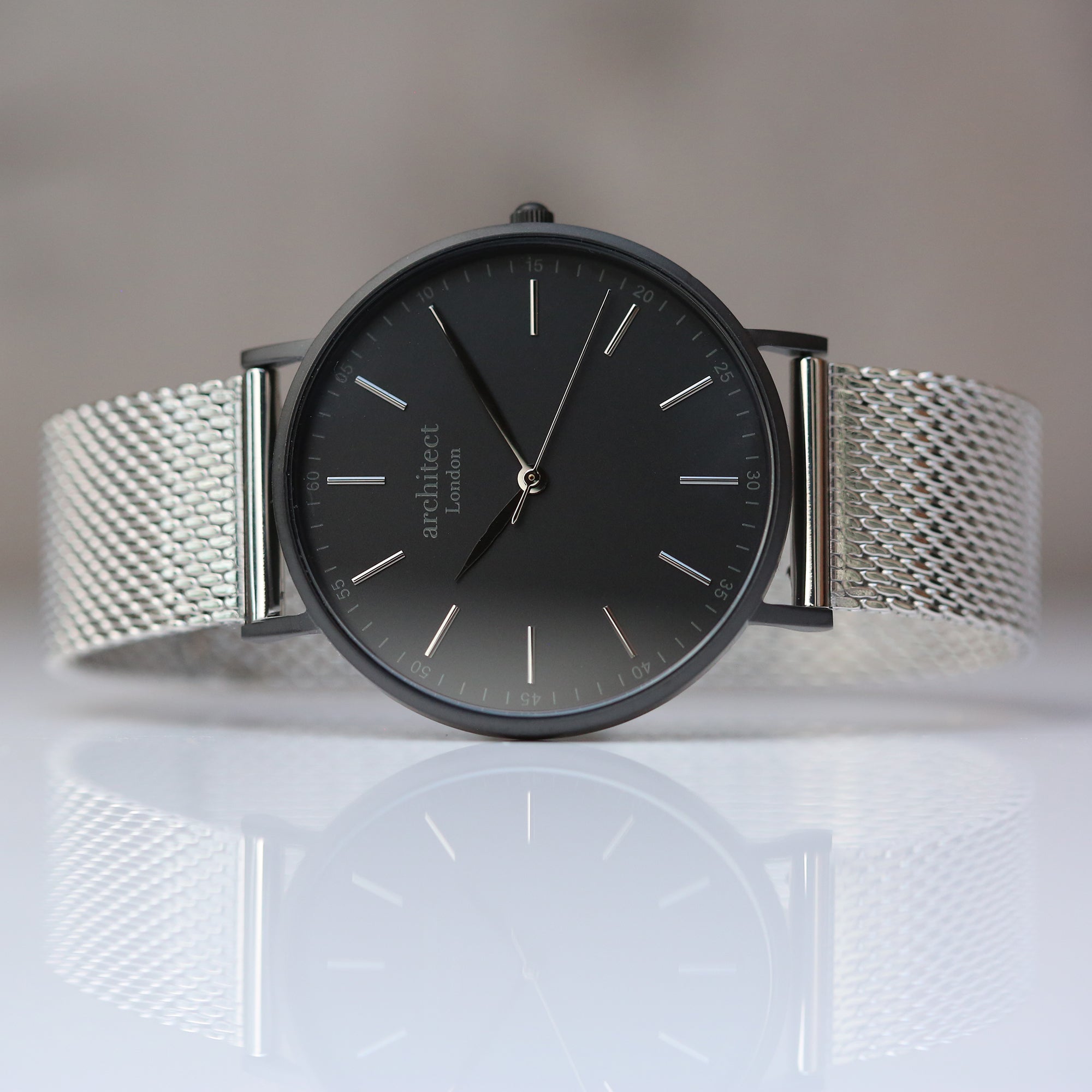 Wristwatch with black dial and silver mesh band on a reflective surface