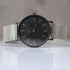 Wristwatch with black dial and silver mesh band on a reflective surface