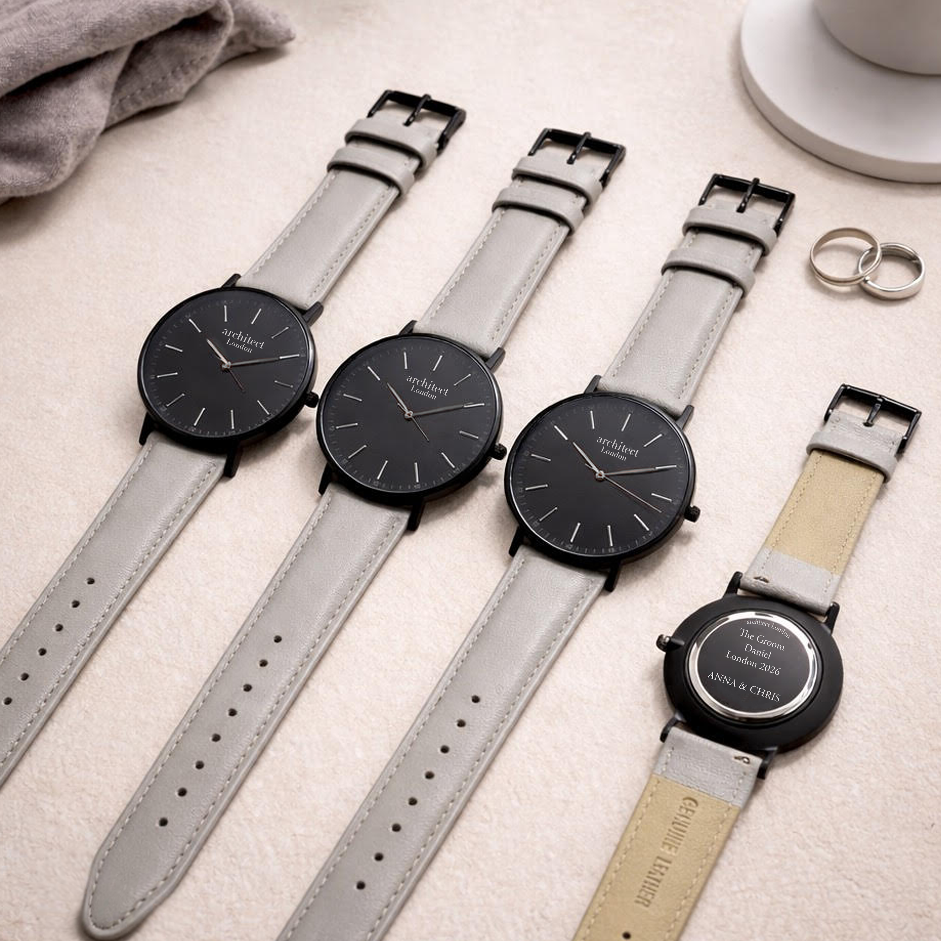 Four minimalist watches with light grey straps, one showing engraved back