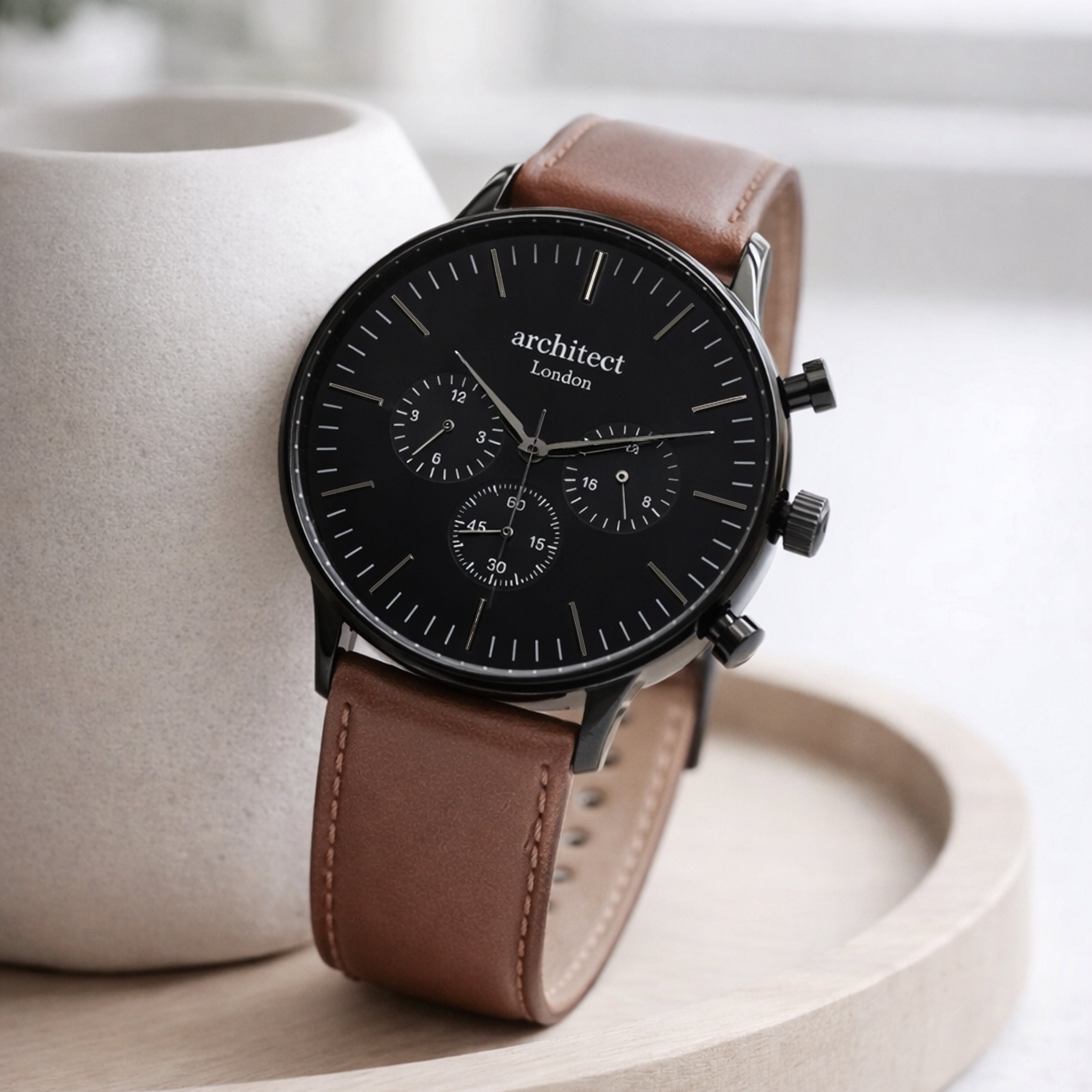 Watch with brown leather strap and black face on a light background engraved at the back