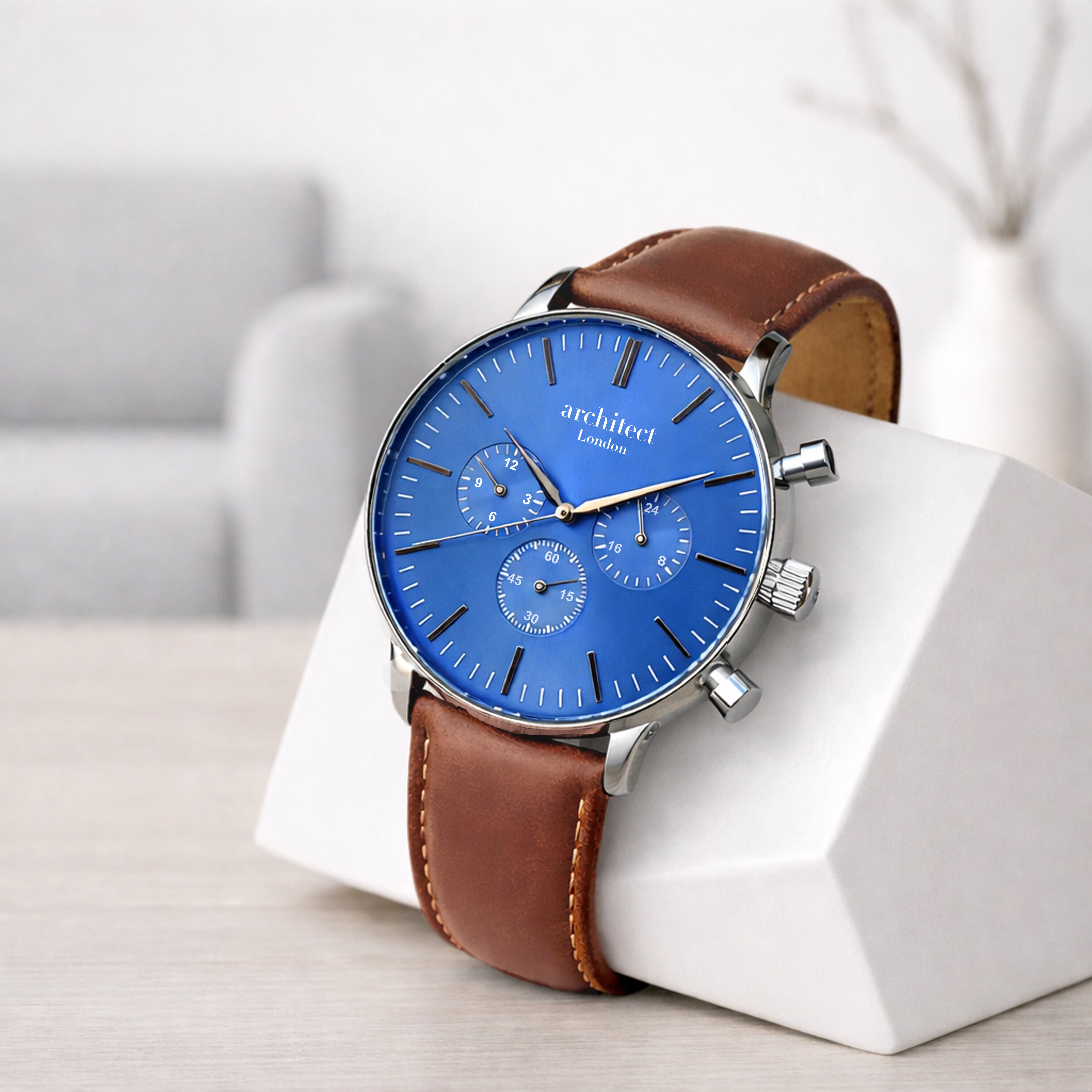 Watch with blue face and brown leather strap on a white stand