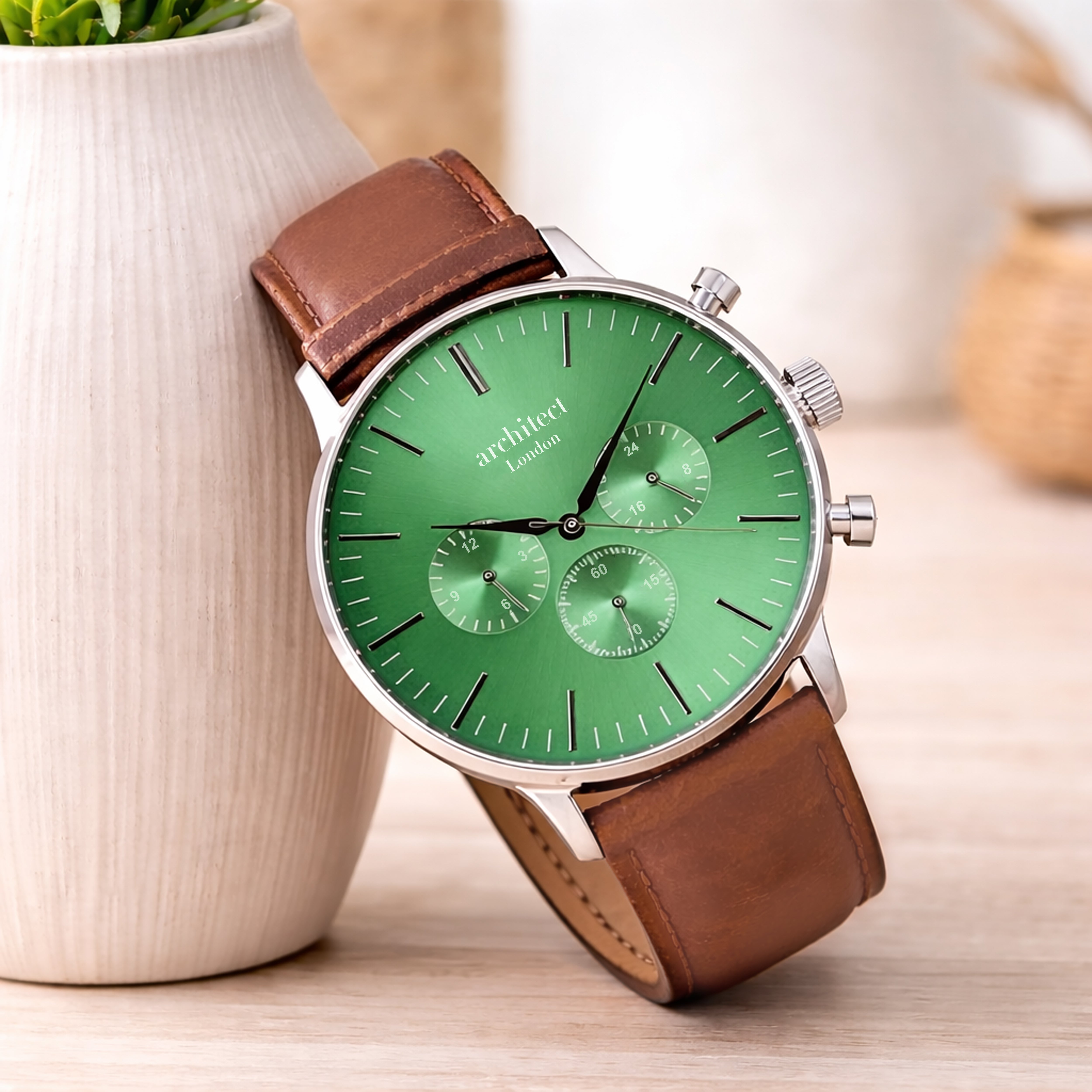 Green watch with brown leather strap on a wooden surface