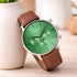 Green watch with brown leather strap on a wooden surface