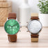 Two engraved watches with green and beige faces on a wooden surface.
