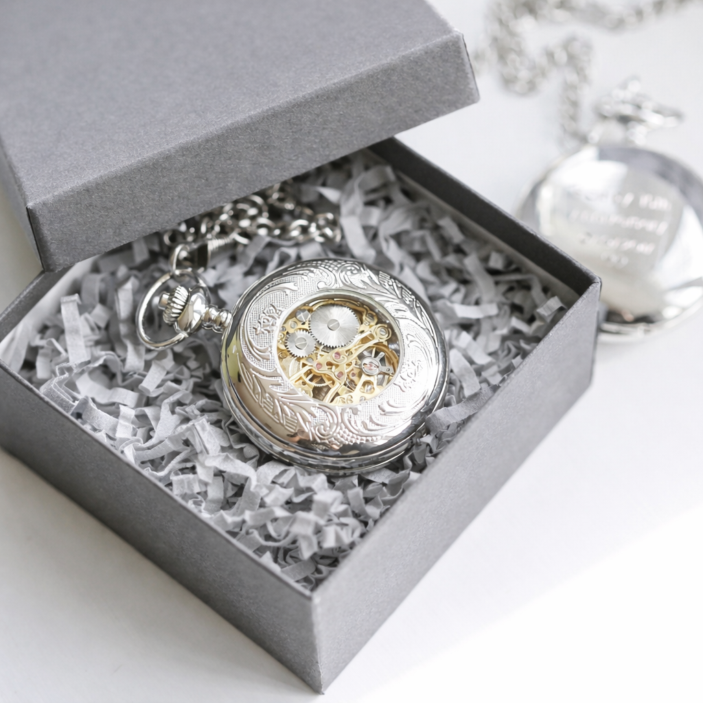 Silver pocket watch with intricate design in a gray gift box