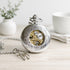 Ornate silver pocket watch with engraved case and visible mechanical skeleton movement