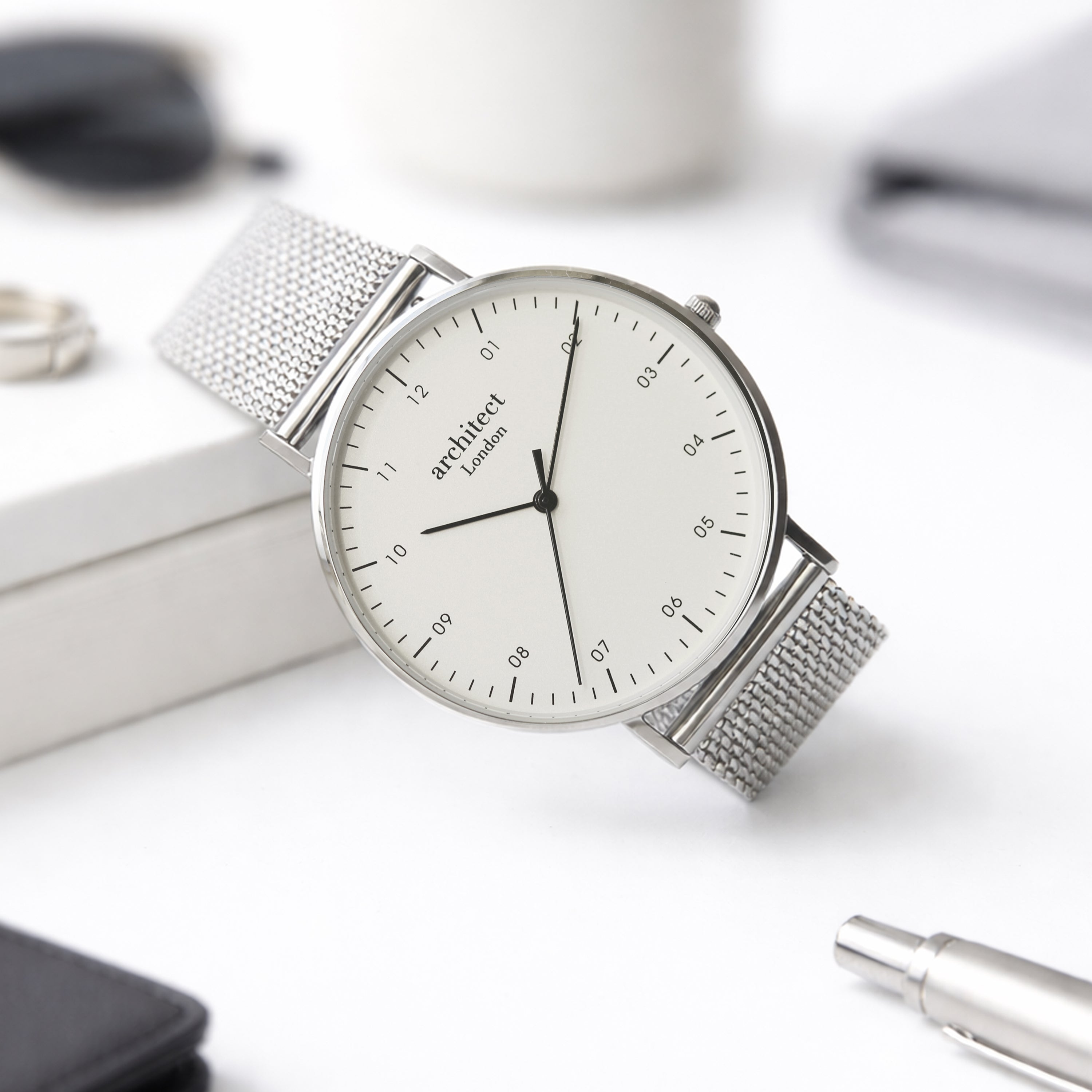 Silver watch with a white face on a light surface with office items.